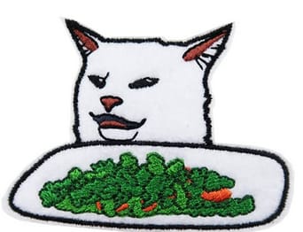 Cat looking confused next to a plate of salad internet meme done as an embroidered patch 